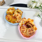 Two small pastries shaped like bears on a white plate with flowers in the background.